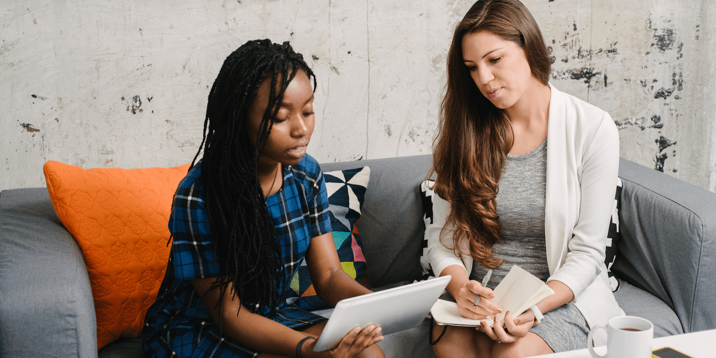 person conducting a user experience interview, taking notes as the participant interacts with a tablet